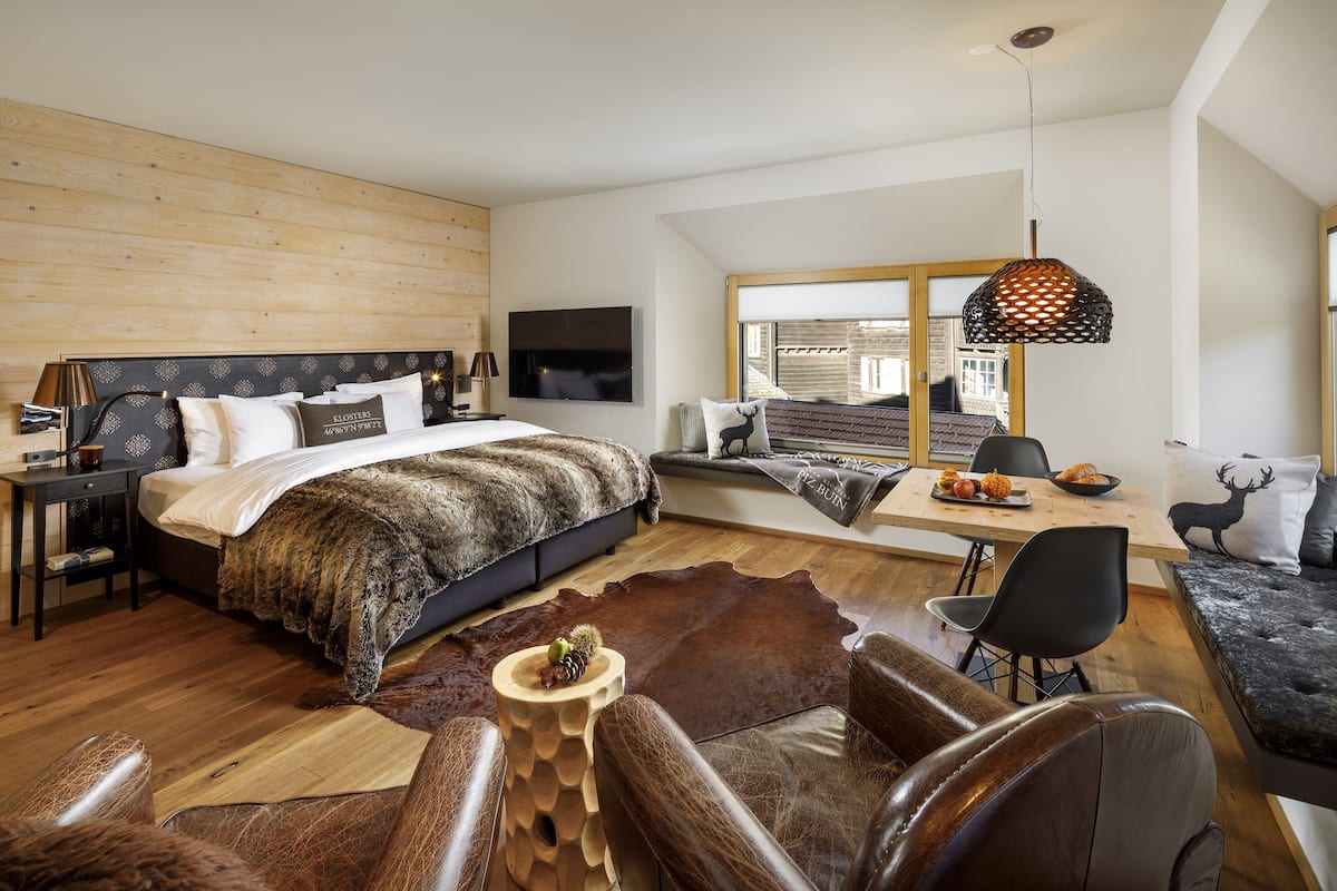 Ein modernes Schlafzimmer mit einem großen Bett, einem Holzkopfende, einem Fernseher, einem Schreibtisch mit Stuhl und einem Ledersofa.