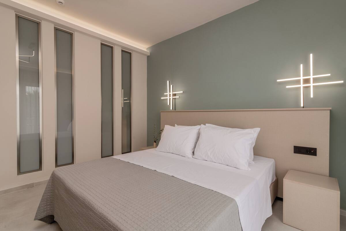 A modern bedroom with a large bed, a nightstand, and a wall-mounted light fixture.
