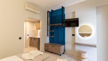 A modern bedroom with a bed, a wooden dresser, a TV, and a round mirror.