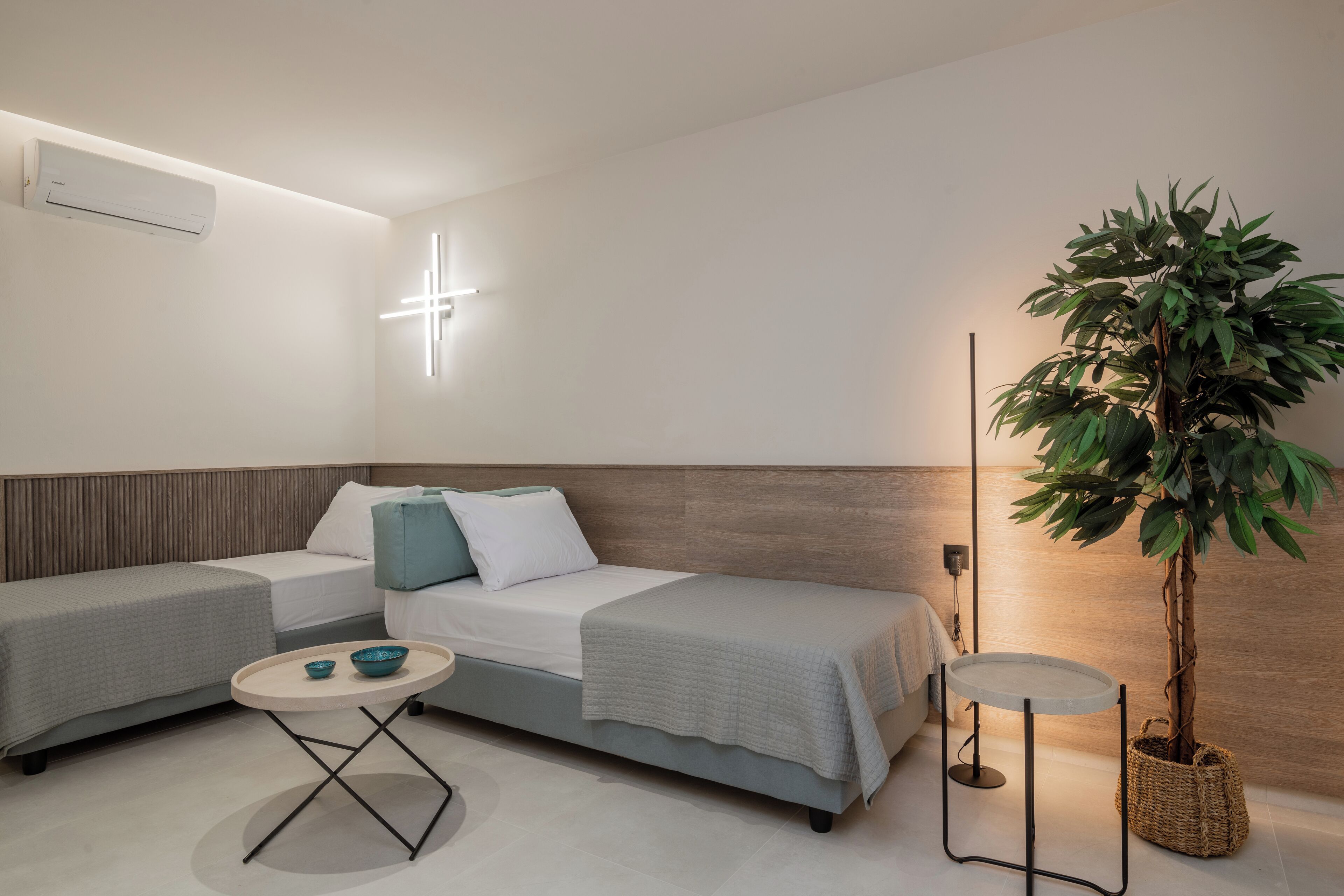 A modern hotel room with a bed, two sofas, a small table, and a potted plant.