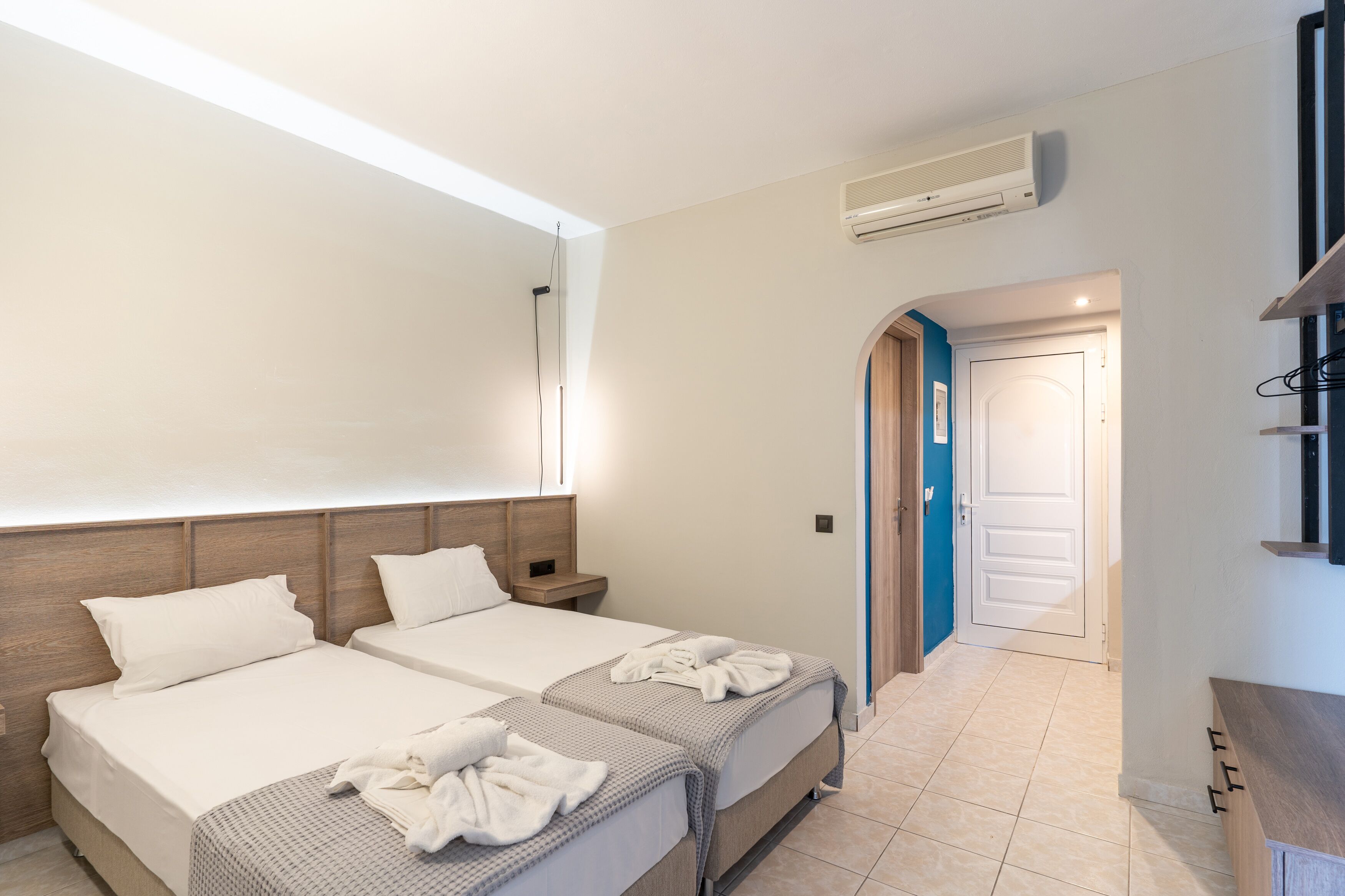 A hotel room with two beds, a wooden headboard, a built-in air conditioning unit, and a bathroom door with a blue frame.
