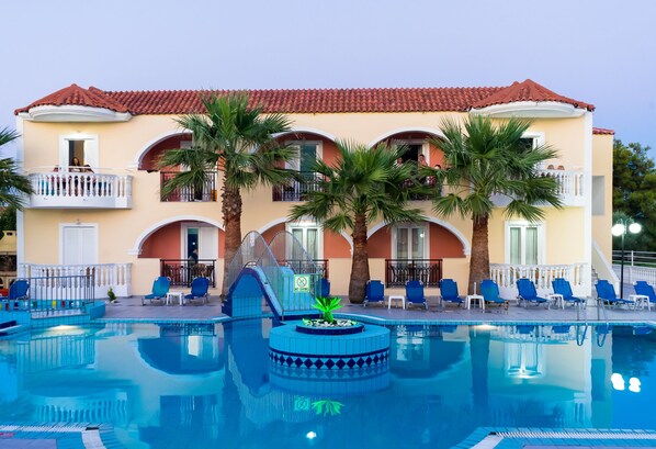 A hotel with a swimming pool, palm trees, and blue lounge chairs. - Hera Zakynthos Hotel (Zakynthos)