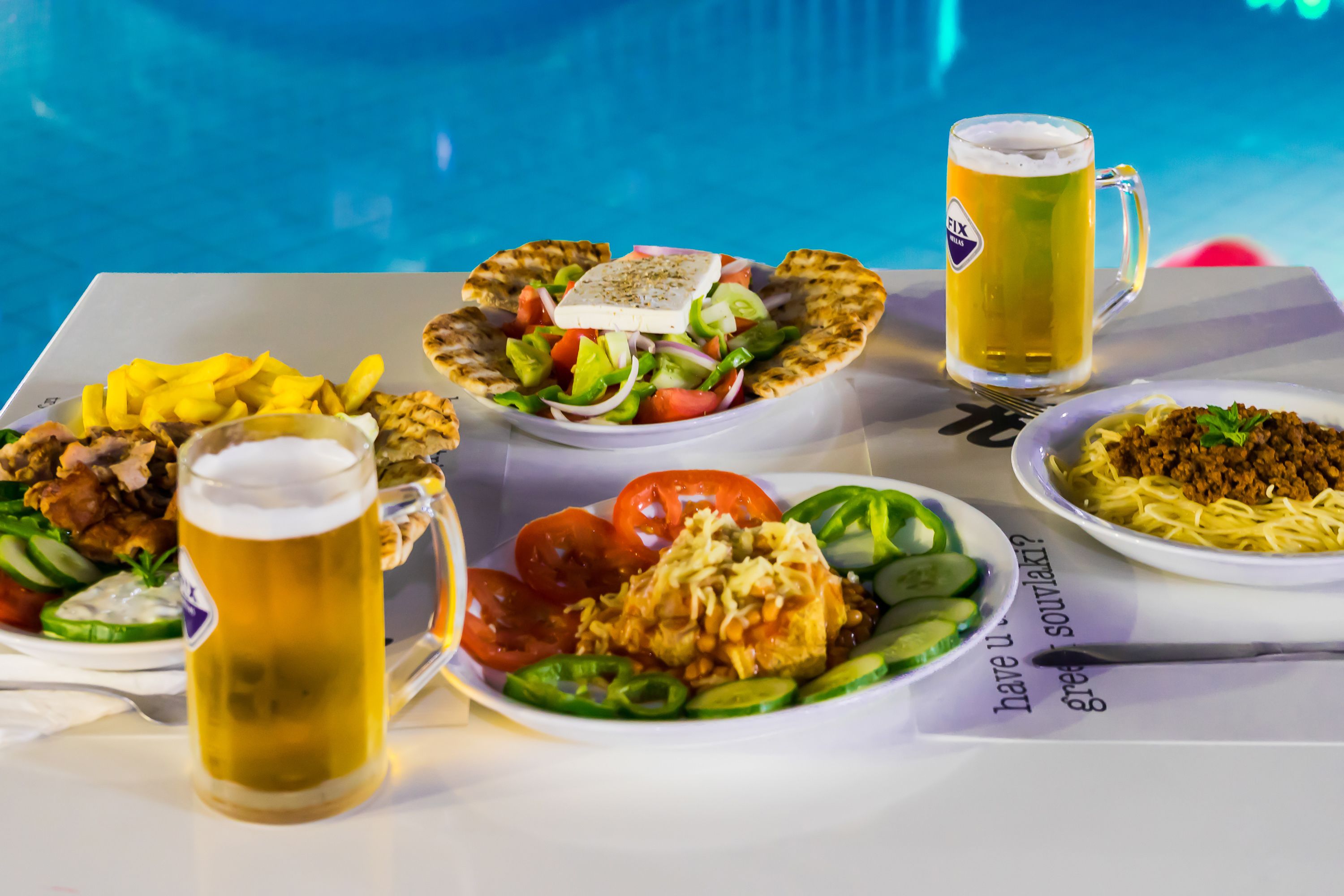Een tafel met diverse gerechten, een bierglas en een zwembad.