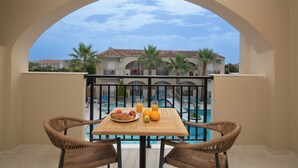 A balcony with a table set for breakfast, overlooking a swimming pool and a building with palm trees. - Hera Zakynthos Hotel (Zakynthos)