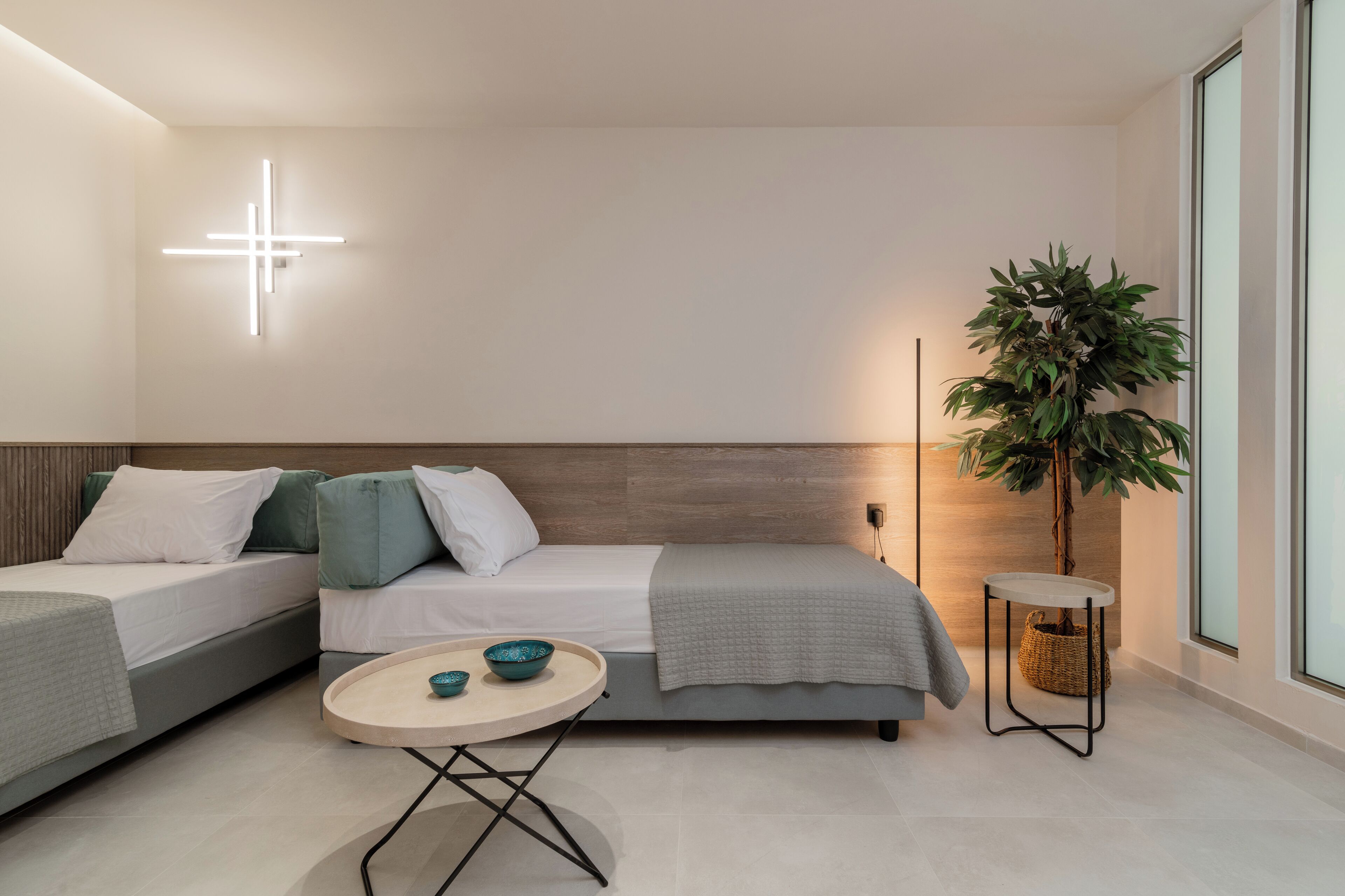 A modern, minimalist bedroom with two beds, a round table, and a large plant.