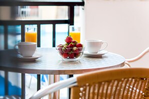 A breakfast setting with a bowl of strawberries, two glasses of orange juice, and two white cups on a round table. - Hera Zakynthos Hotel (Zakynthos)