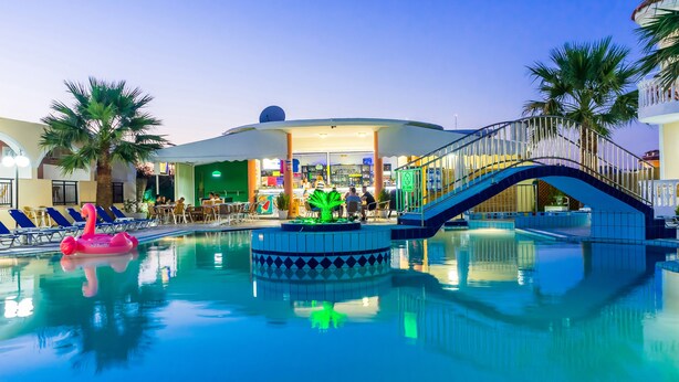 A pool area with lounge chairs, a pink flamingo float, a green decorative fountain, and a staircase leading to a covered area with a bar and seating. - Hera Zakynthos Hotel (Zakynthos)