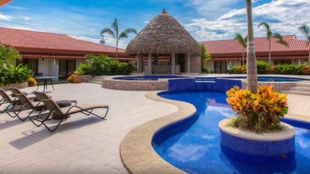 A resort with a swimming pool, lounge chairs, and a thatched-roof structure. - Hotel Coclé (Penonome)
