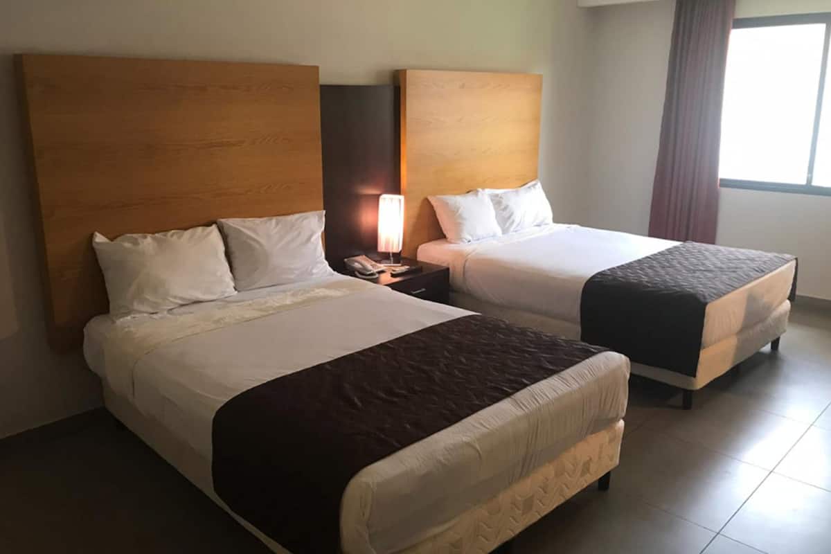 A hotel room with two beds, each with a wooden headboard, white bedding, and a brown throw blanket.