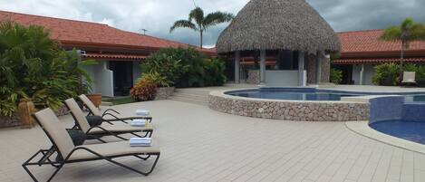 A resort pool area with lounge chairs, a thatched-roof structure, and a stone wall.