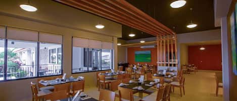 Un restaurante con varias mesas y sillas, ventanas amplias y vistas al exterior.
