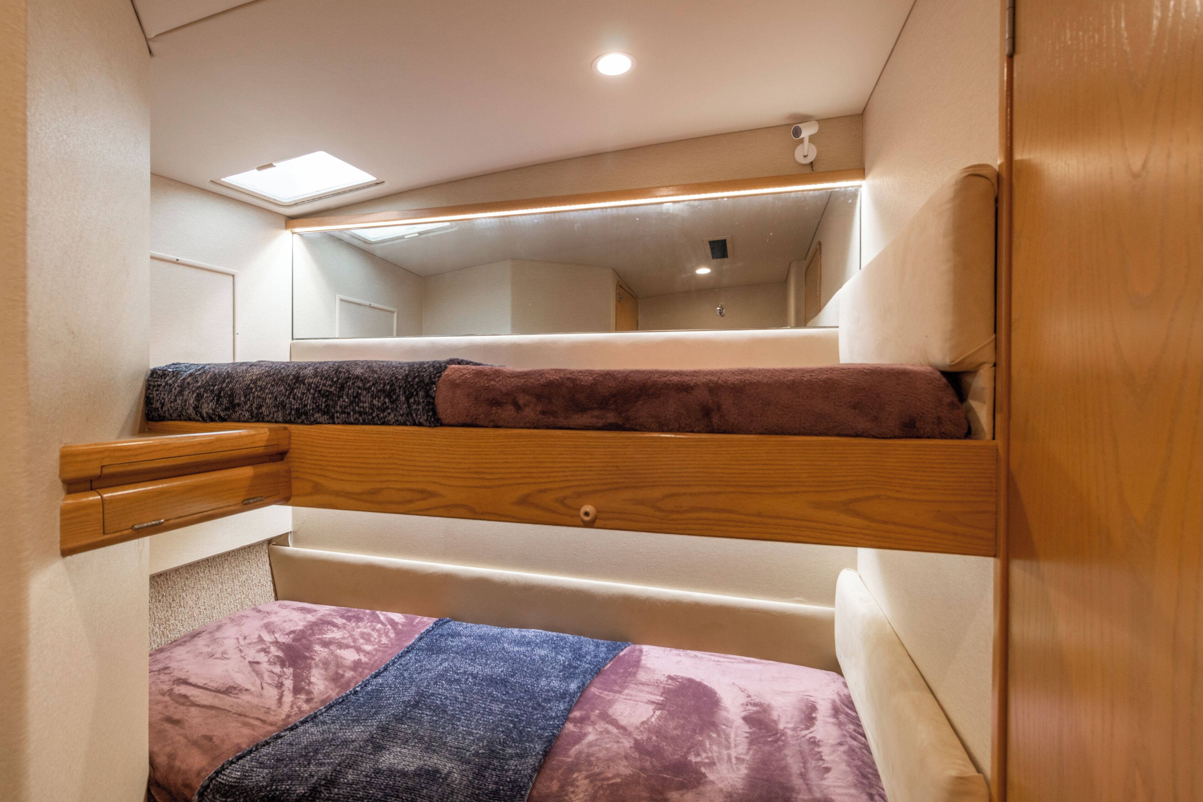 A bunk bed with a skylight above, wooden headboard, and a mirror on the wall.