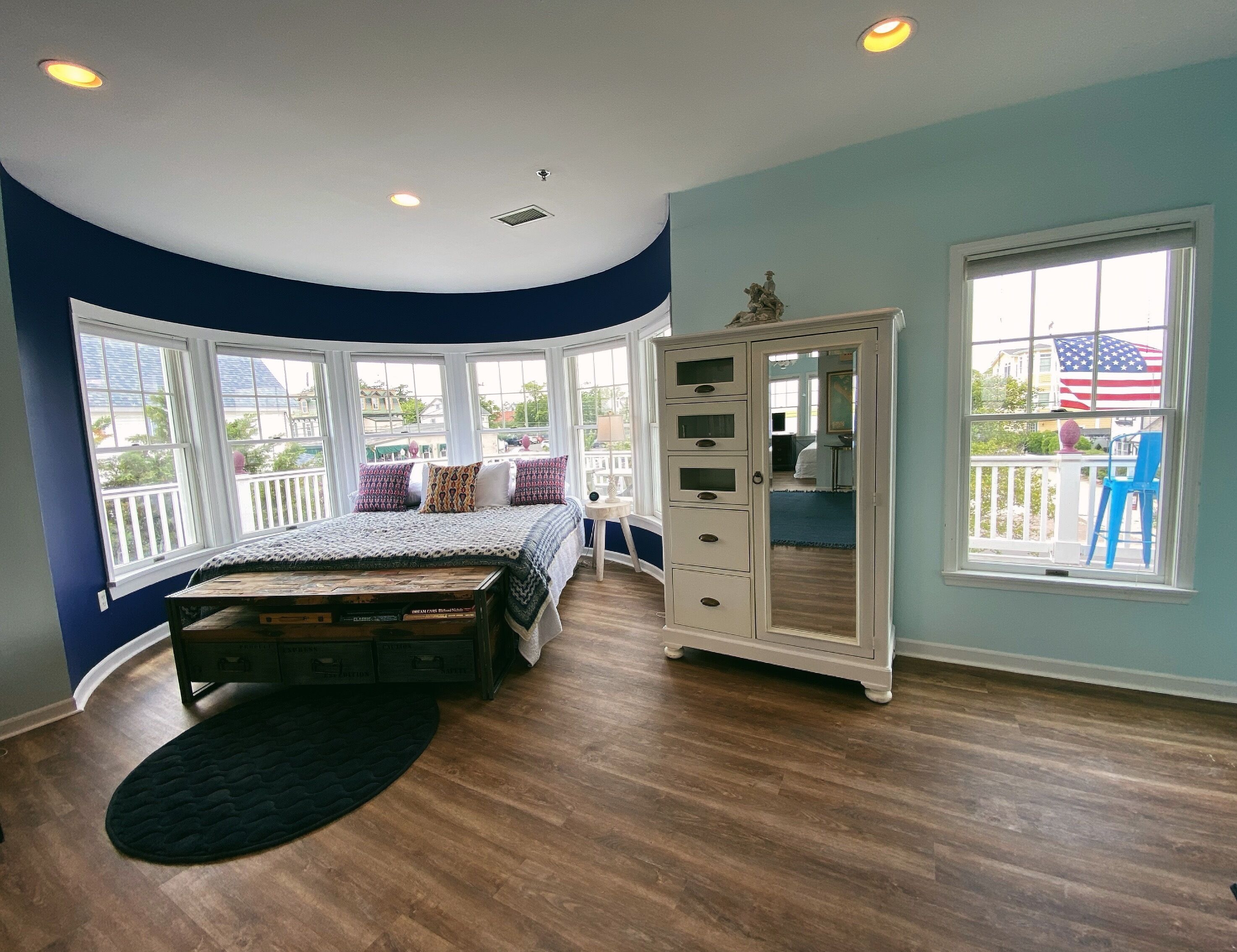 A bedroom with a curved ceiling, large windows, a bed with patterned bedding, a dresser, and a view of the outside.