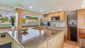 Een moderne keuken met een groot eiland, een ingebouwde magnetron en uitzicht op palmbomen en water.