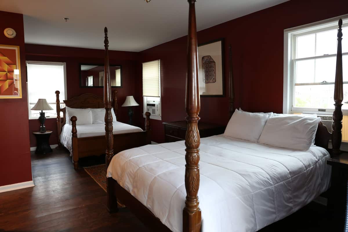 Een hemelbed met witte beddengoed, een houten vloer en een groot raam dat zorgt voor natuurlijk licht.