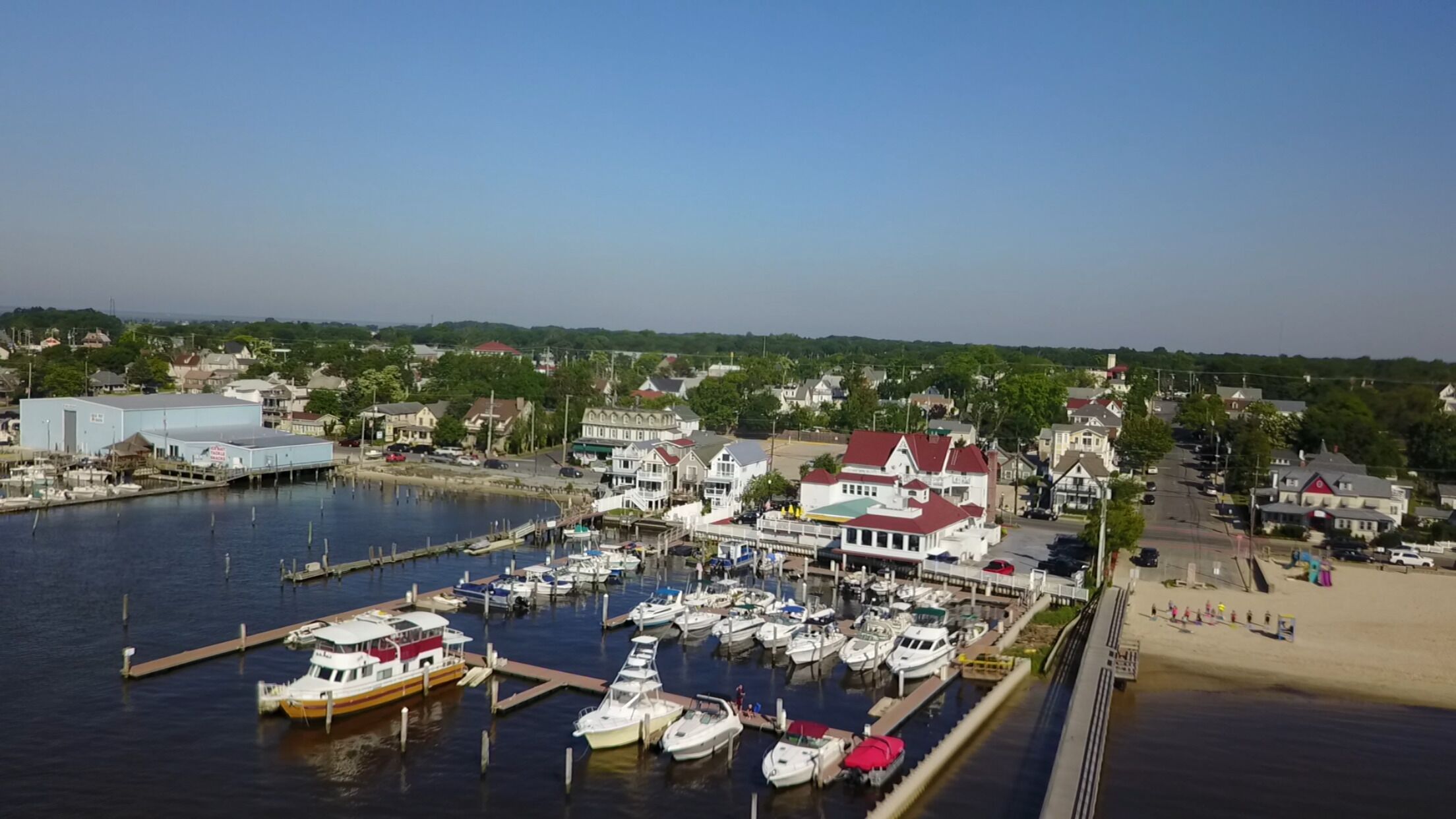 A marina with boats docked, a pier, and residential buildings in the background.