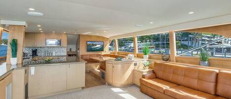A modern kitchen with a central island, a seating area with a sofa, and large windows offering views of the marina.