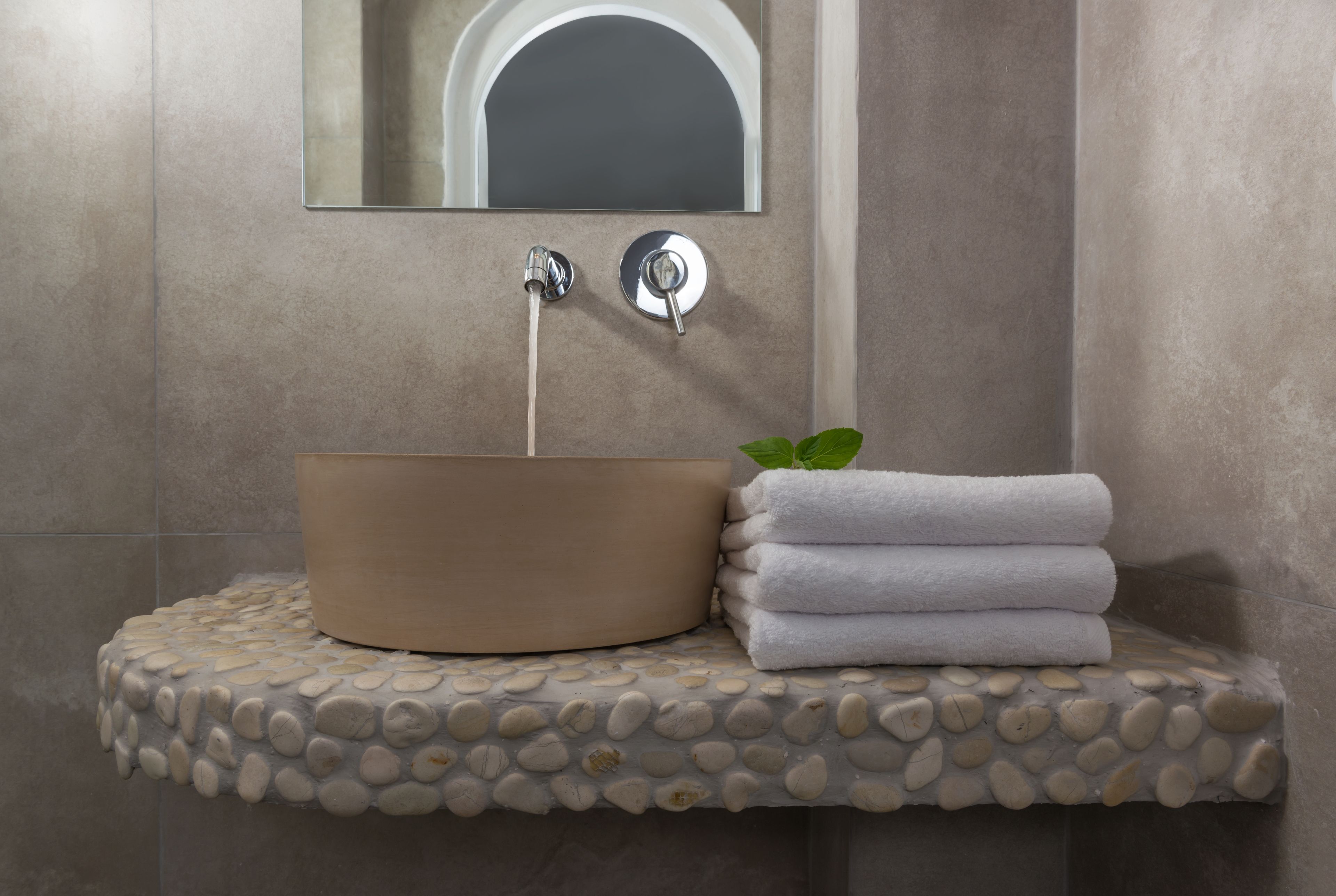 Un baño con un lavabo color beige, un espejo y una pila de toallas blancas sobre un estante con diseño de piedritas.