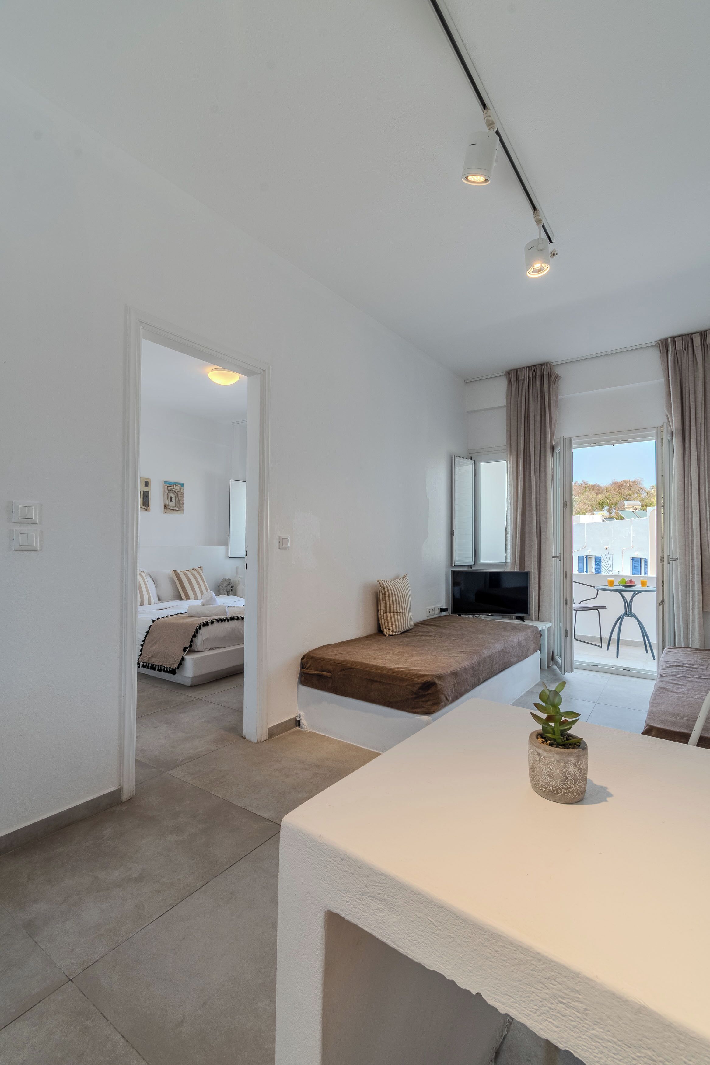 A modern, well-lit room with a bed, a sofa, a TV, and a dining area with a table and chairs.