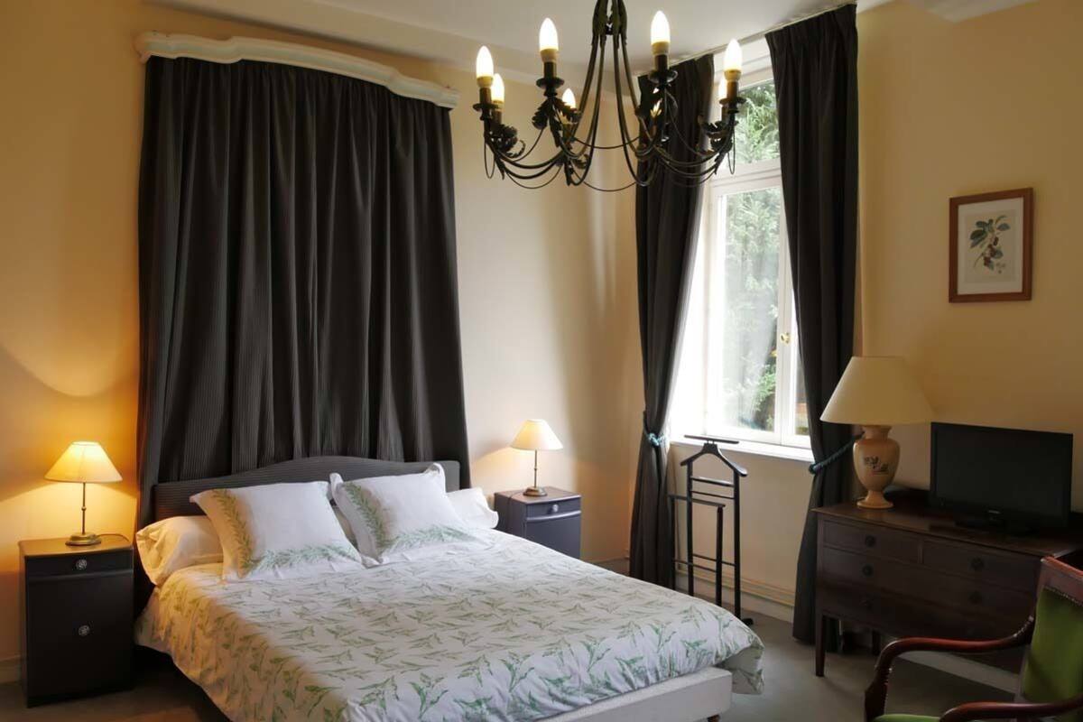 A bedroom with a bed, two bedside tables, a TV, a chair, and a window with curtains.