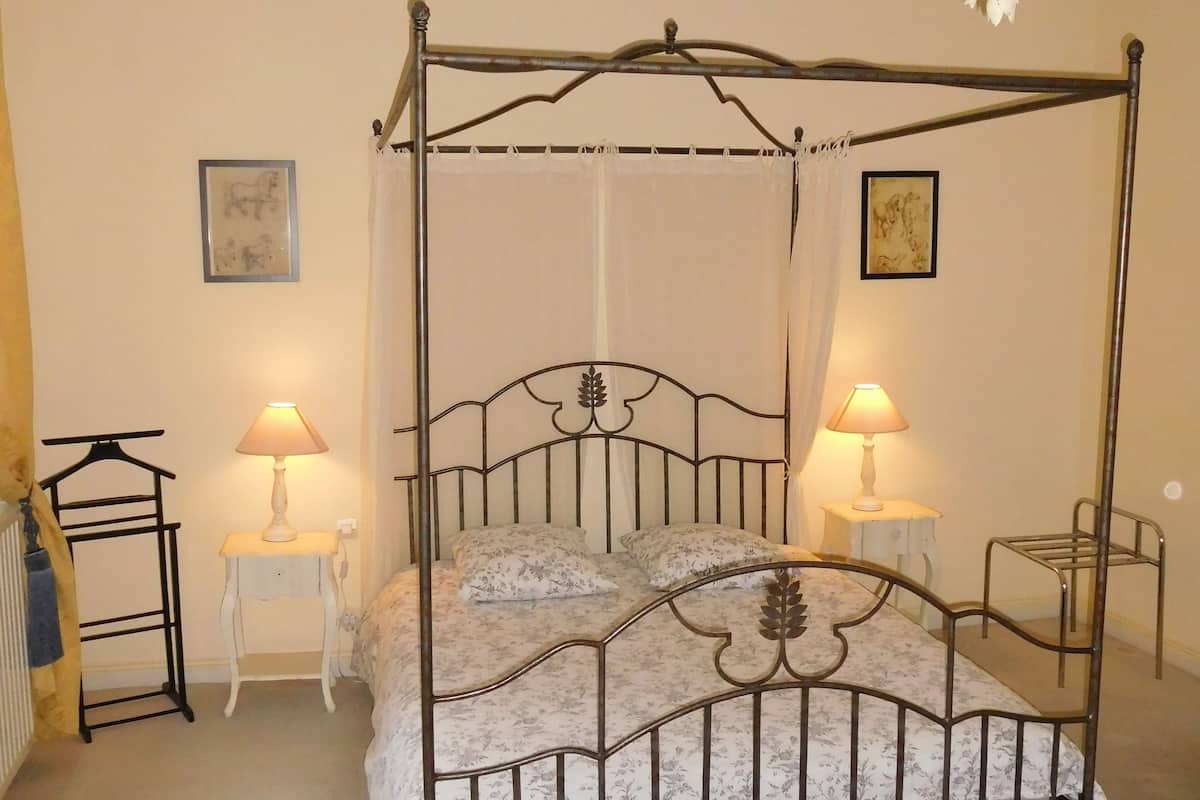 A four-poster bed with a canopy, two bedside tables with lamps, a red patterned rug, and a chandelier.