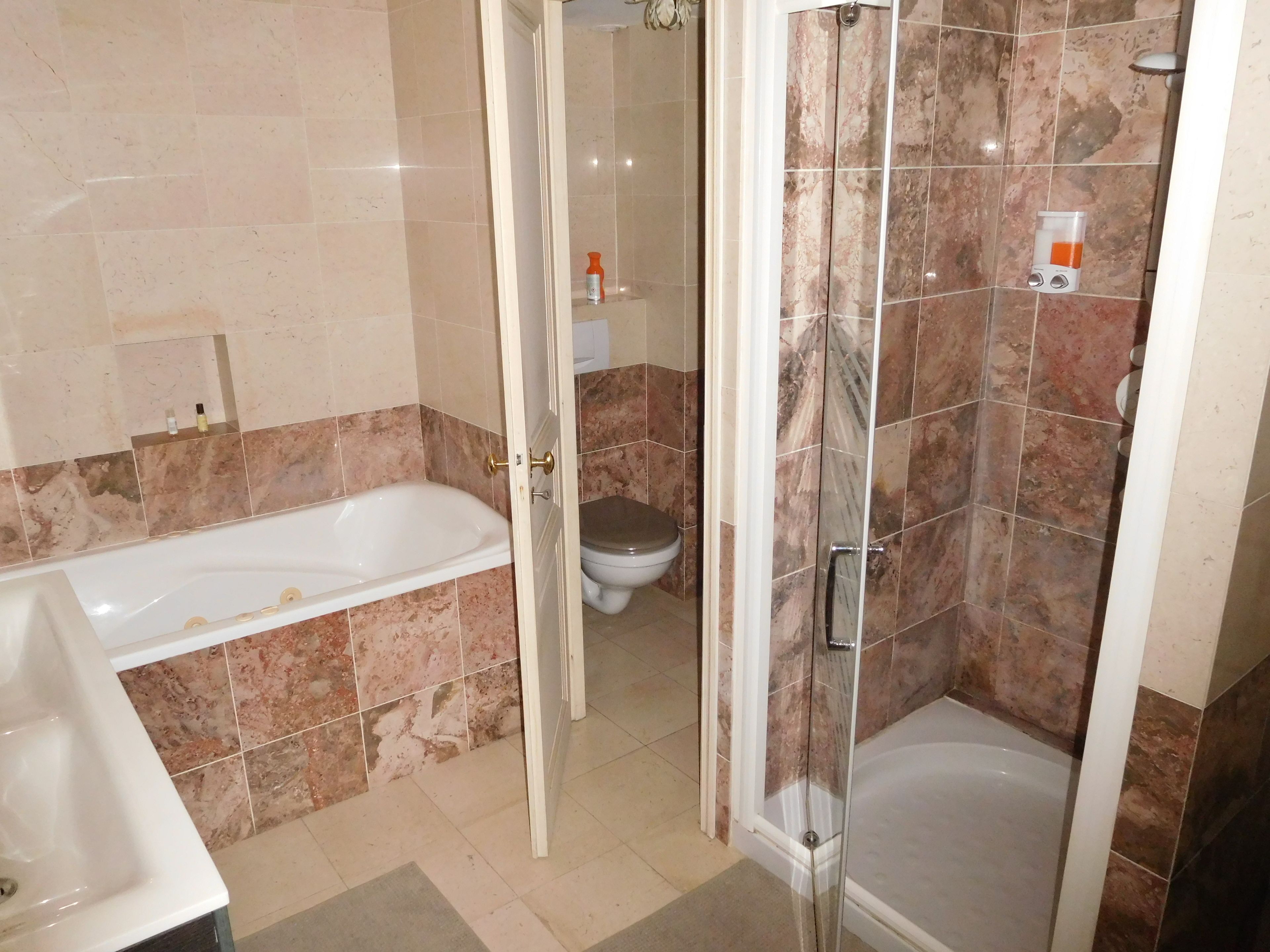 Une salle de bain équipée d’une baignoire, de toilettes et d’une douche séparée par des parois en verre.