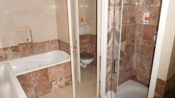 Une salle de bain équipée d’une baignoire, de toilettes et d’une douche séparée par des parois en verre.