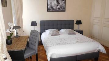 A neatly arranged bedroom with a bed, two bedside tables with lamps, a chair, a small table with a lamp, and a wall-mounted picture.
