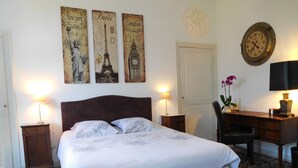 A bedroom with a bed, two bedside tables, a desk, a chair, a clock, and three wall decorations depicting famous landmarks. - Chambres d'Hôtes Château de Courcelette (Lannoy)