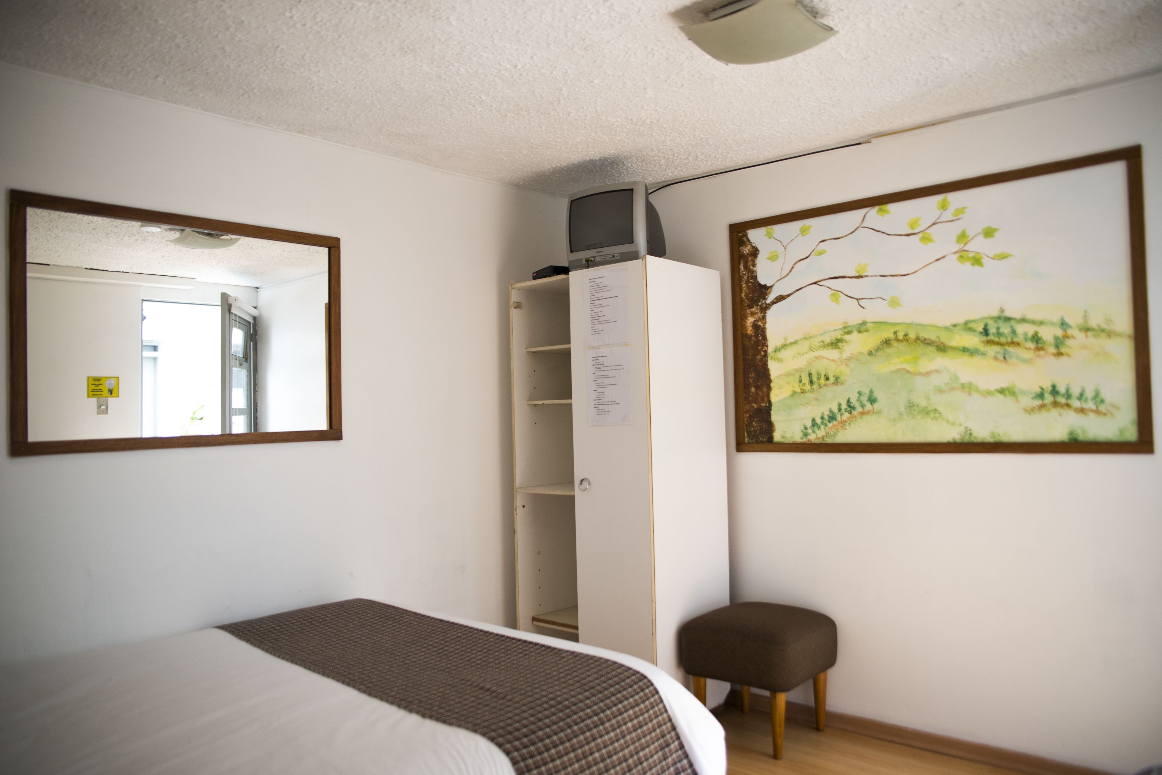 Un dormitorio con cama, armario, silla, un cuadro y un espejo.