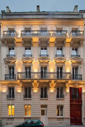 A multi-story building with balconies, large windows, and a red door.