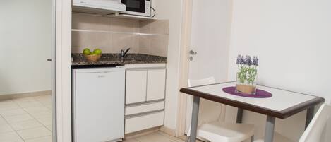 Una cocina compacta con microondas, un refrigerador pequeño y una mesa de comedor con dos sillas.