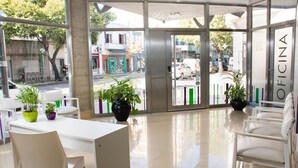 Un espacio de oficina moderno con área de recepción, mobiliario blanco y plantas en macetas.