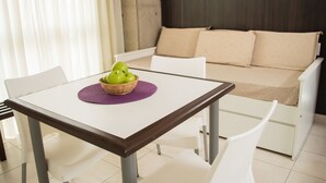 Una habitación moderna con un sofá blanco, una mesa de comedor con camino de mesa morado y una cesta de manzanas verdes.