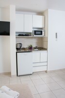 Una cocina compacta con armarios blancos, un microondas, una cafetera y un lavabo.