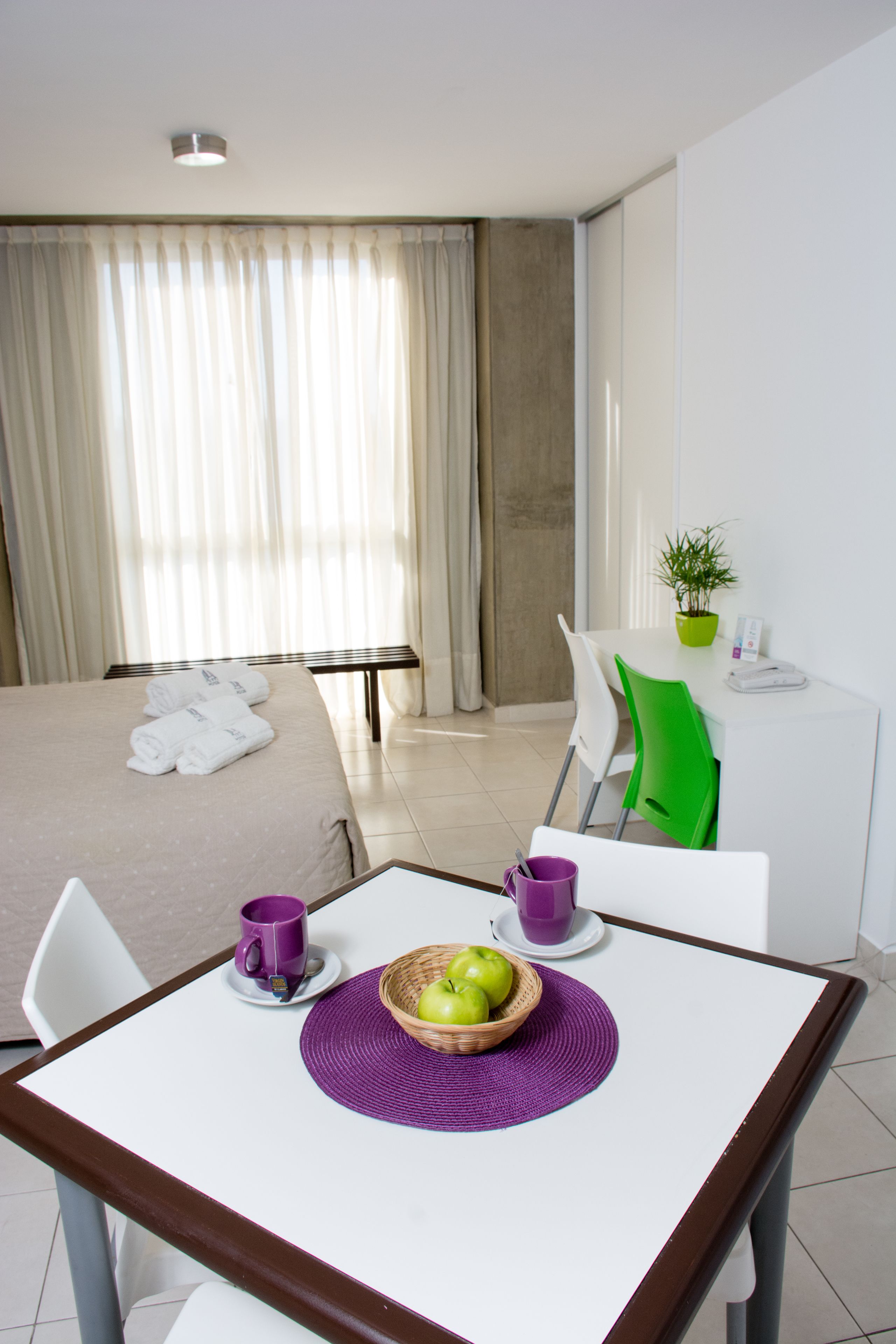 A hotel room with a bed, a desk, a chair, a table, and a window with curtains.