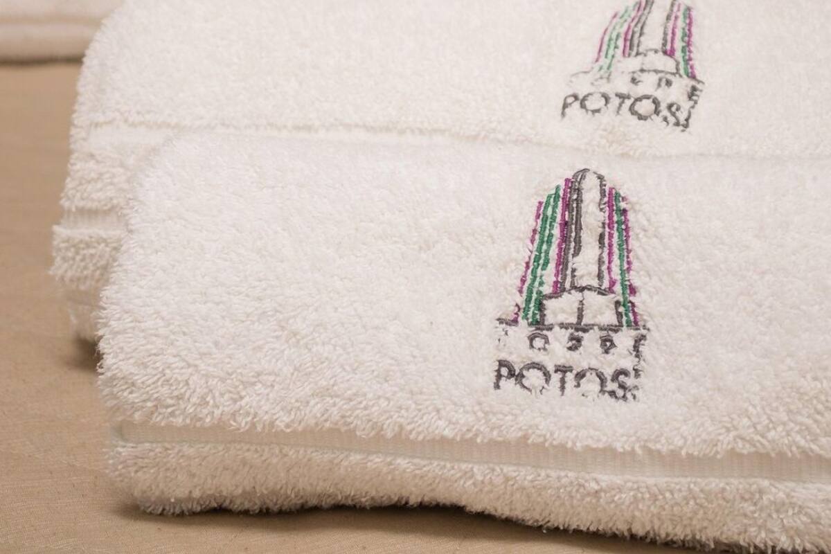 Toallas blancas dobladas con logotipos bordados sobre una superficie color crema.
