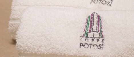 Neatly folded white towels with embroidered logos on a beige surface.