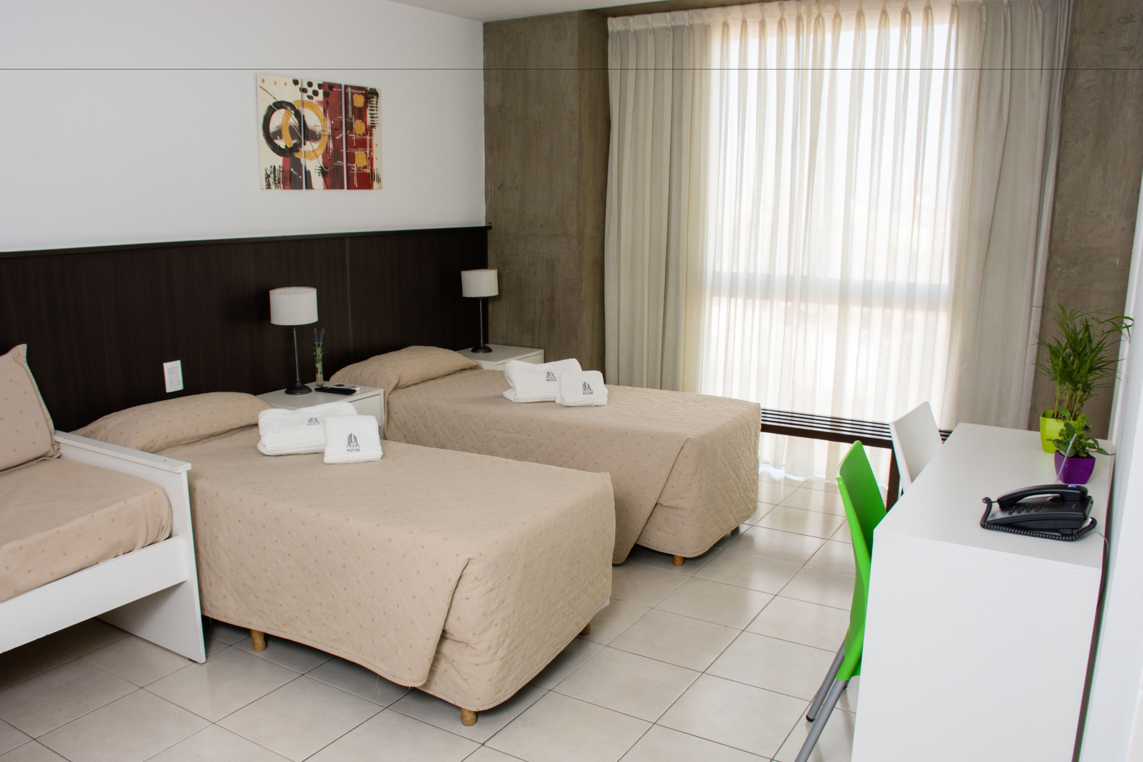 A hotel room with two beds, a desk, a chair, a lamp, a phone, and a plant.