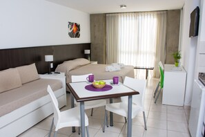 Habitación de hotel con cama, sofá, mesa de comedor con sillas, una pequeña kitchenette y televisor.
