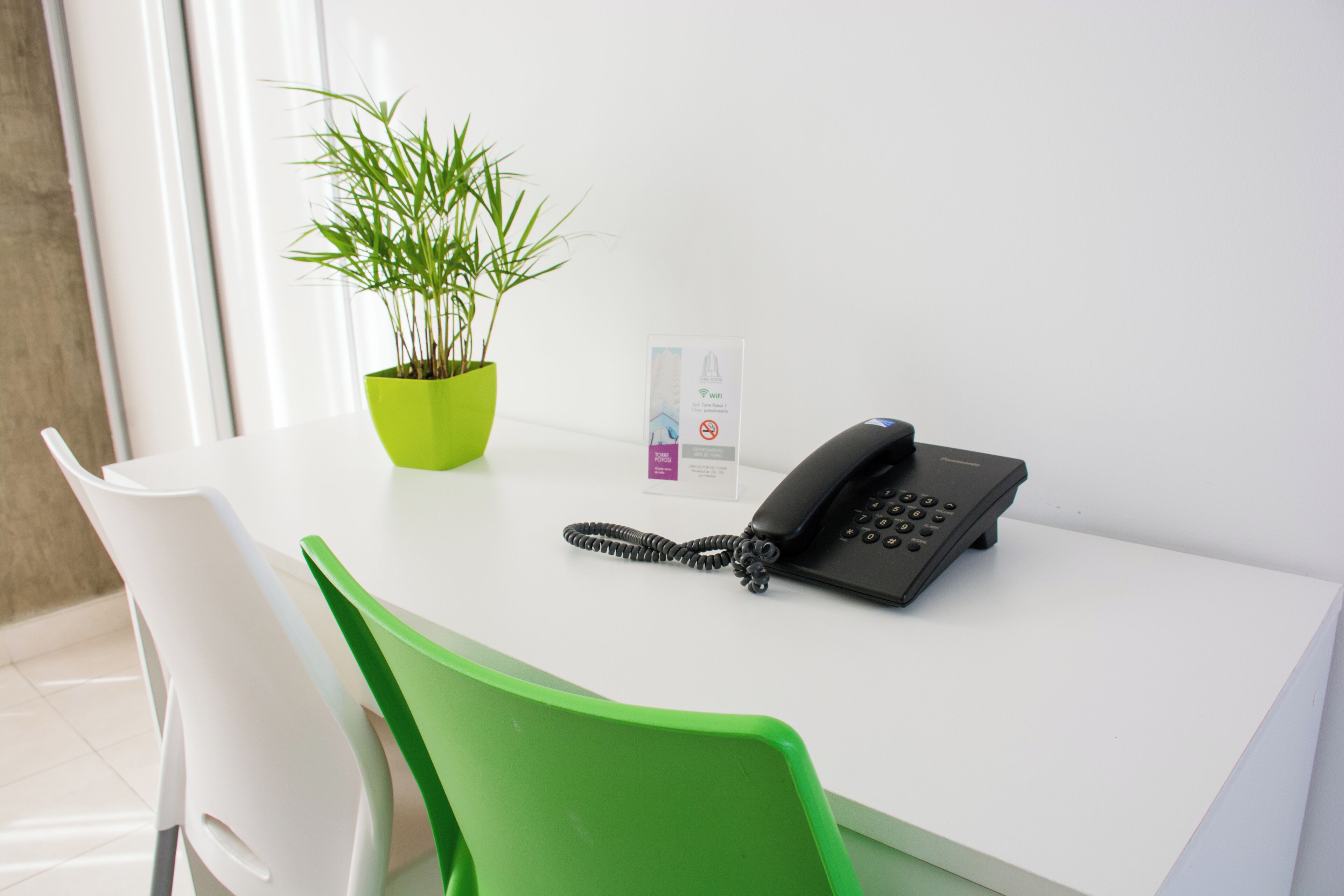 A white desk with a black telephone, a green plant in a green pot, and a sign with a no-smoking symbol.