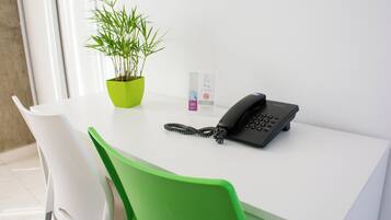 A white desk with a black telephone, a green plant in a green pot, and a sign with a no-smoking symbol.
