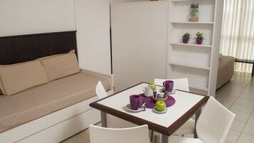 Een moderne woonkamer met een bank, een eettafel met stoelen, een boekenkast en een raam met gordijnen.