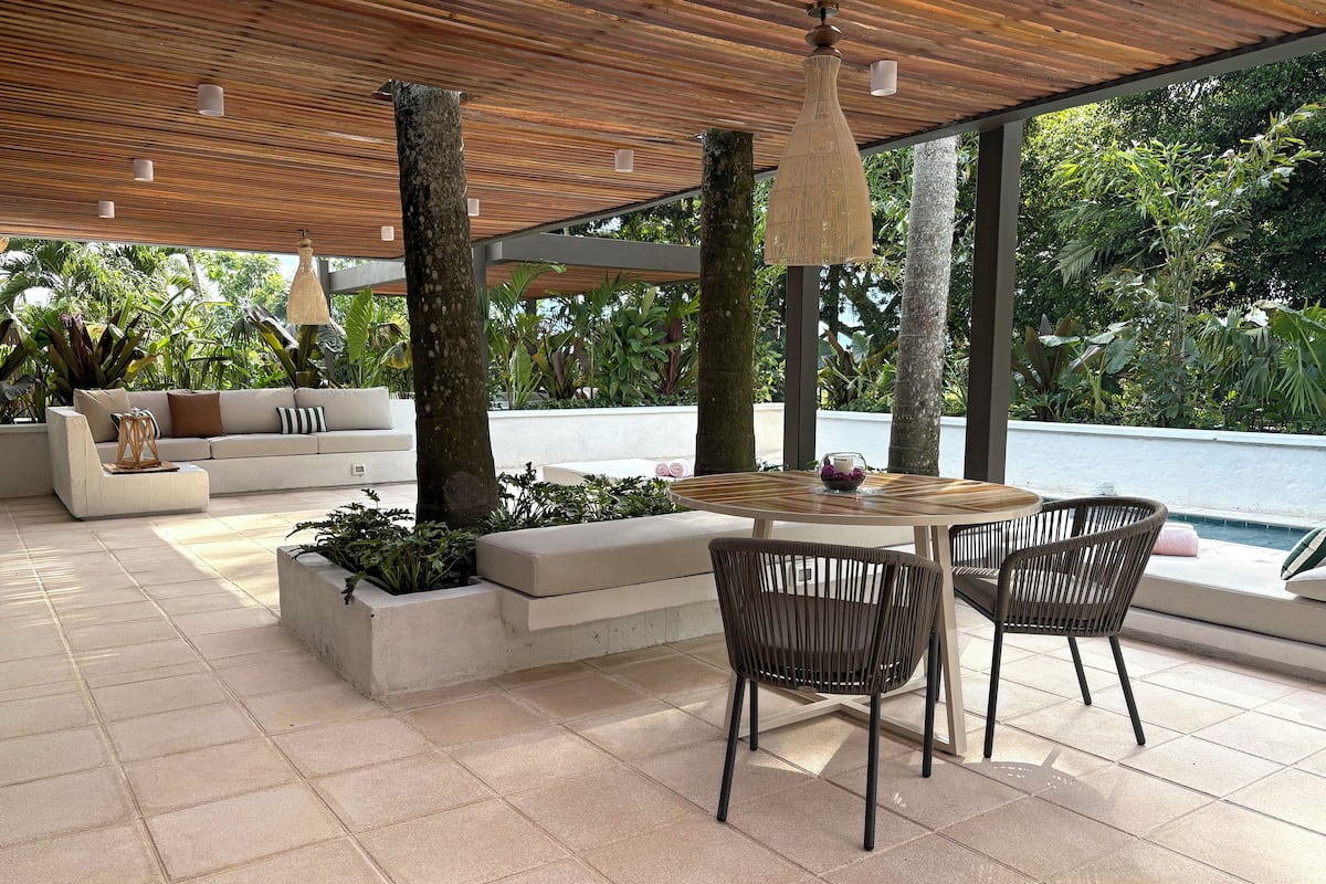 Une terrasse extérieure avec une table ronde, deux fauteuils en osier, un canapé et une vue sur une piscine.