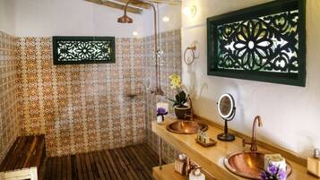 Un baño con baldosas estampadas, un banco de madera, un lavamanos de cobre, un espejo y paneles decorativos en la pared.