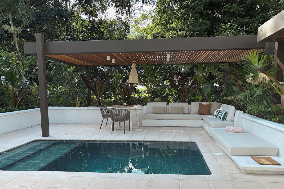 Un espace piscine extérieur moderne, doté d’un coin salon intégré et entouré d’une végétation luxuriante.