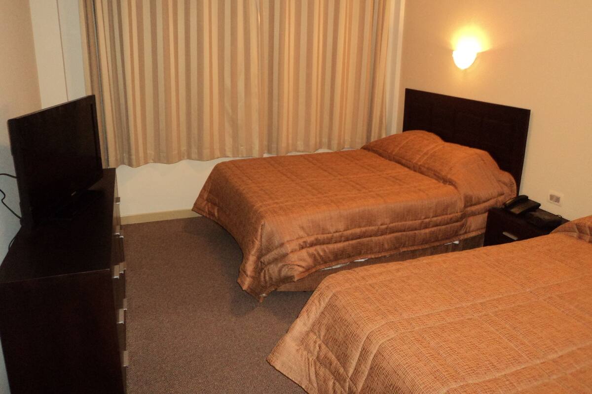 A hotel room with two beds, a TV, and a nightstand.