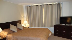 Habitación de hotel con una cama grande, un televisor en una cómoda, una lámpara y una ventana con cortinas.