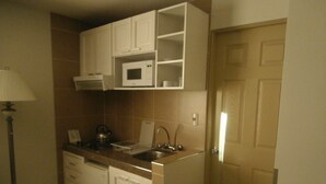 Cocina compacta con armarios blancos, microondas, hervidor y lavabo.