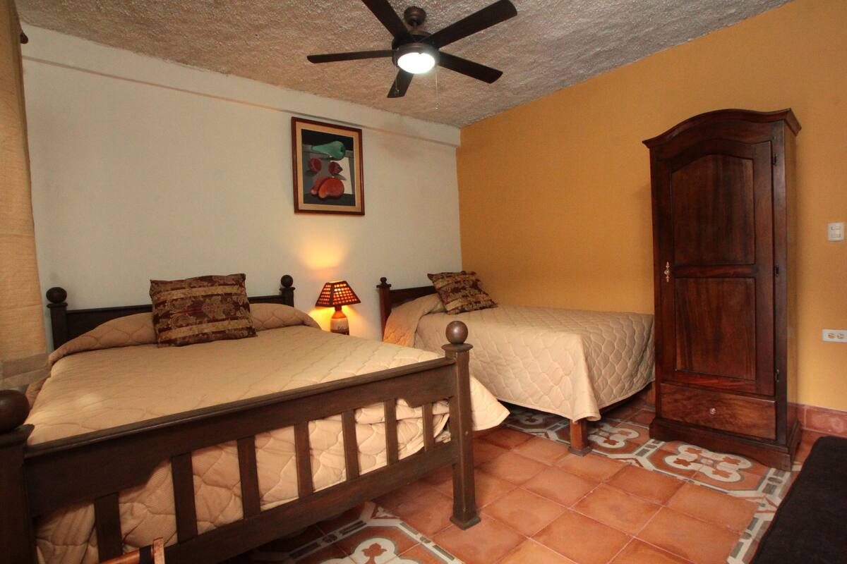 A bedroom with two beds, a ceiling fan, a nightstand with a lamp, and a wardrobe.
